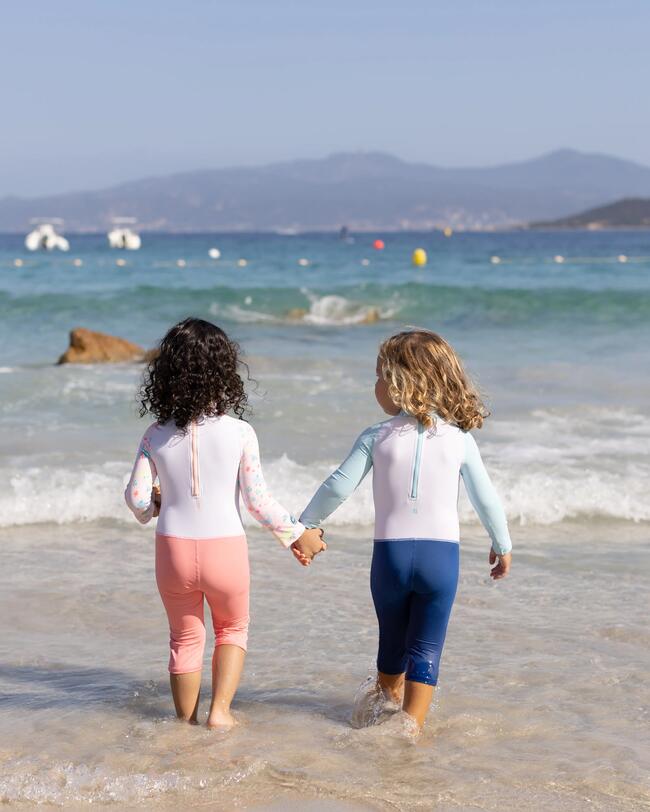 Zwei Kinder rennen händehaltend ins Wasser, UV-Schwimmanzüge