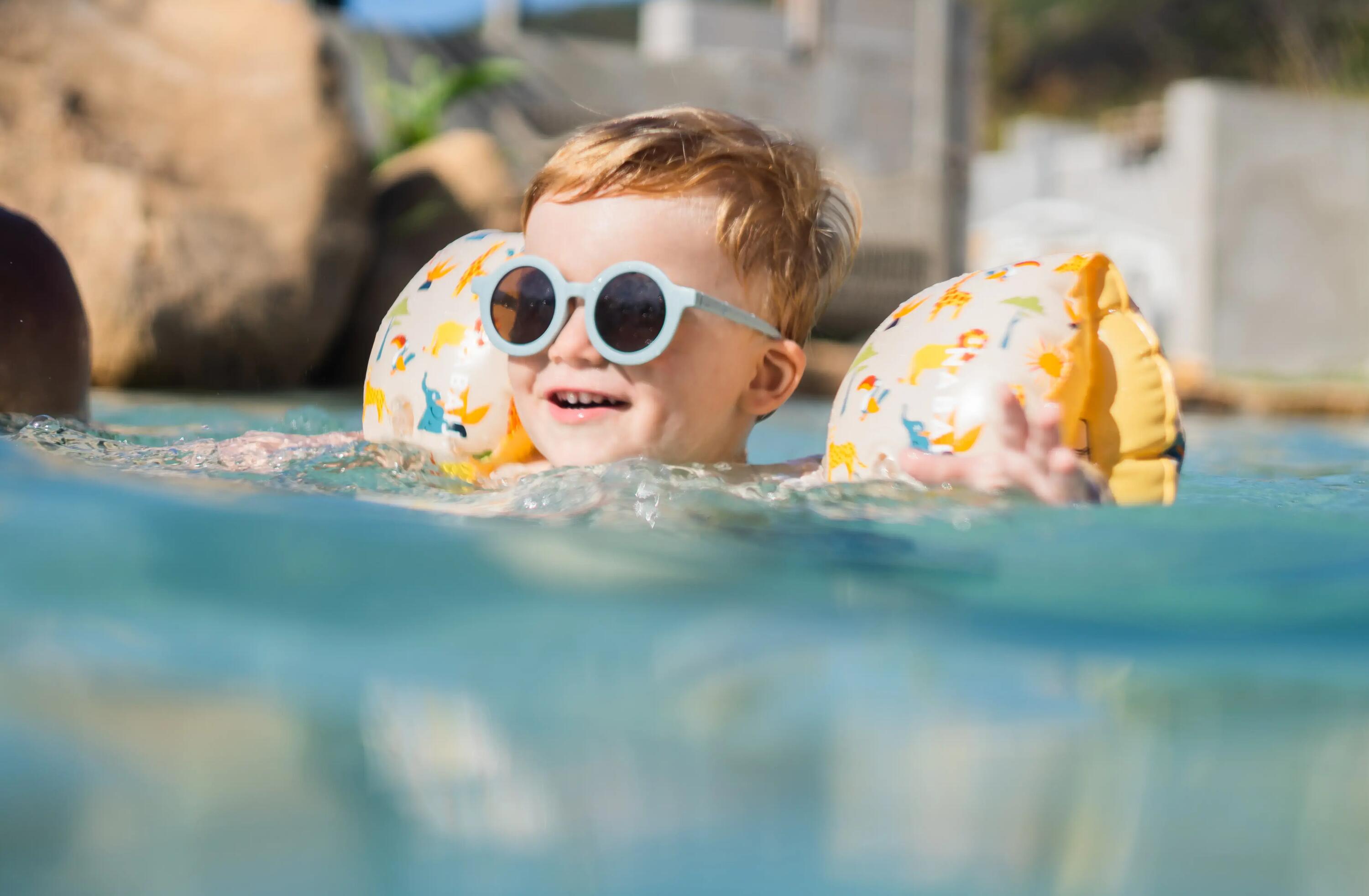 Kind schwimmt mit Schwimmflügeln und Sonnenbrille