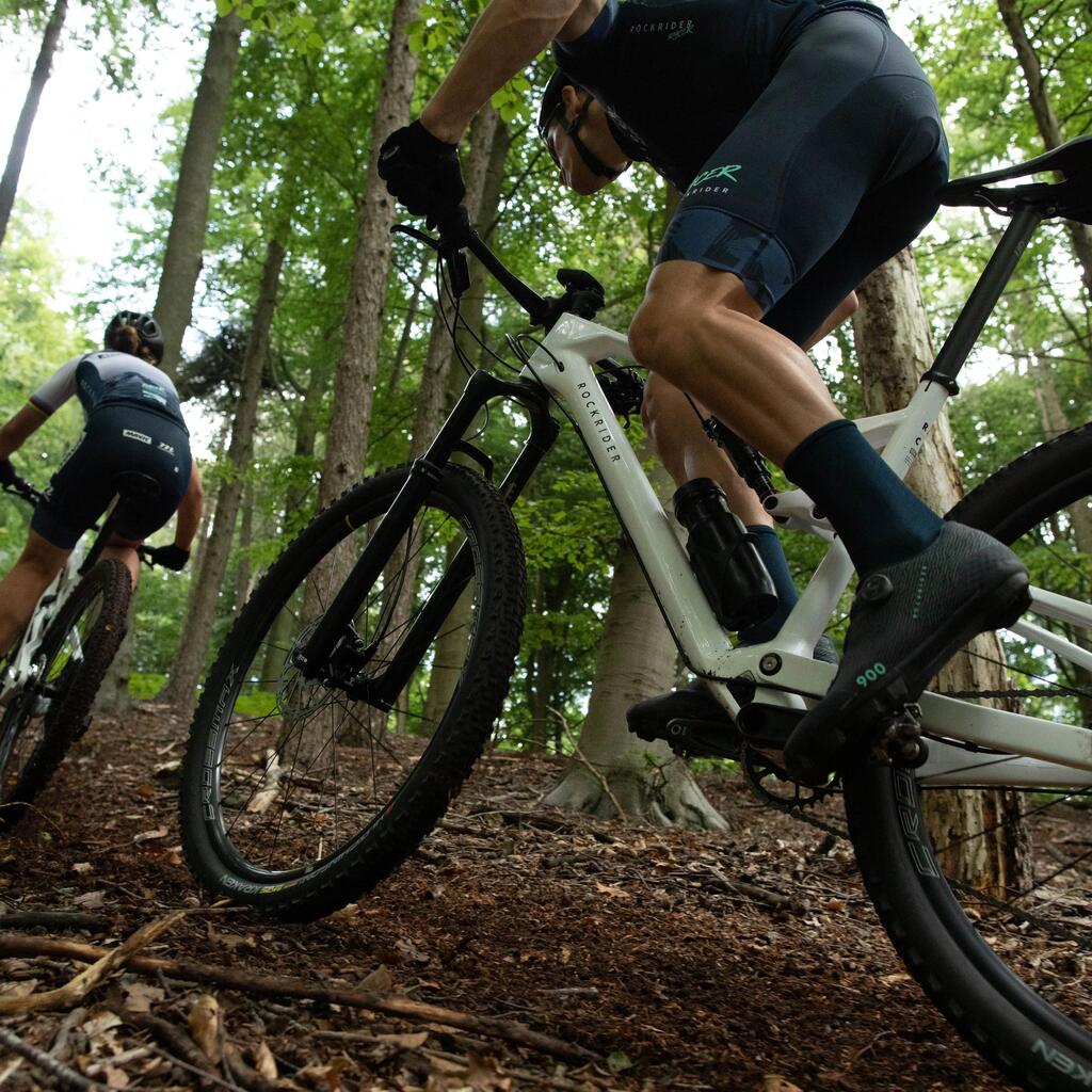 Dvojica biciklista s kacigama voze brdske bicikle Rockrider po šumskoj stazi.