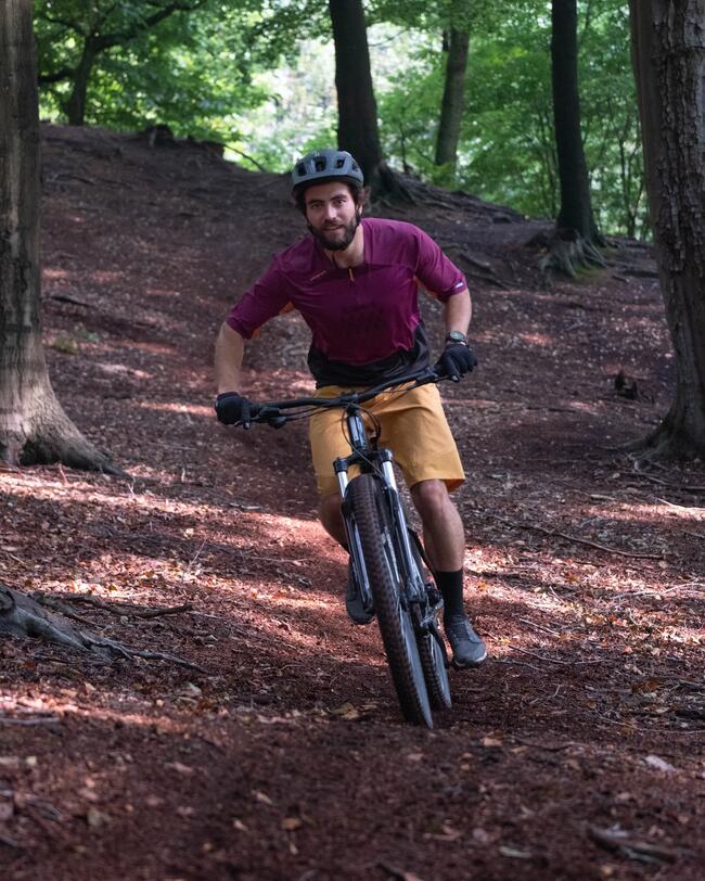 Mann mit schwarzem Helm fährt auf schwarzem Fahrrad mit Laub bedeckten Waldweg entlang