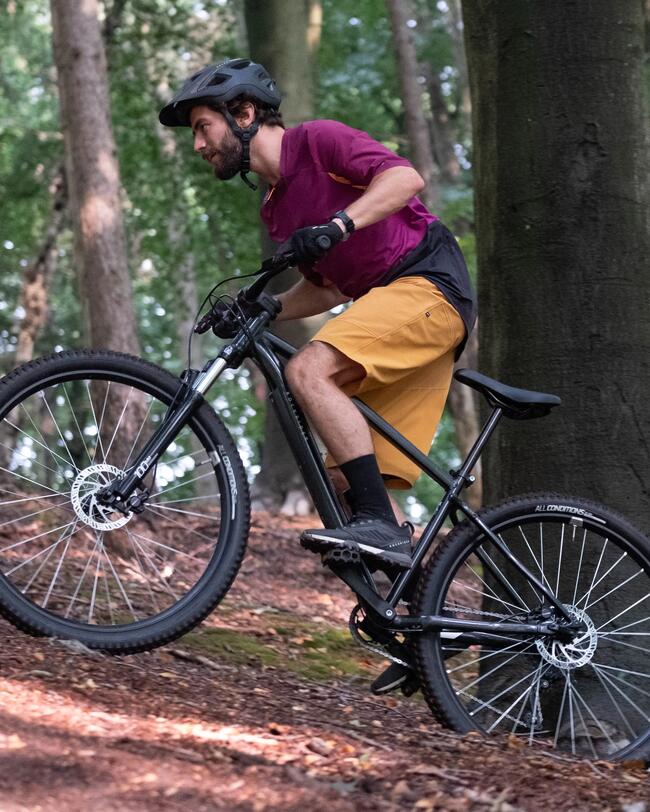 Mann mit schwarzem Helm fährt auf schwarzem geländegängigen Fahrrad einen steilen Waldweg hinauf