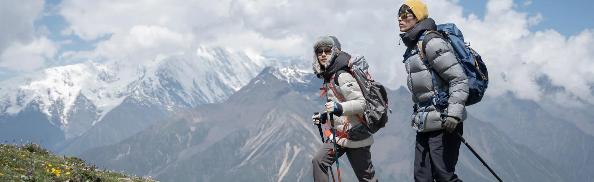osoby wędrujące po górach w kurtkach puchowych trzymając kije trekkingowe w rękach