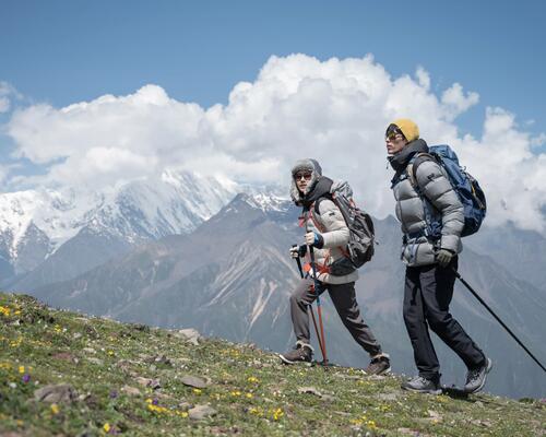 osoby wędrujące po górach w kurtkach puchowych trzymając kije trekkingowe w rękach