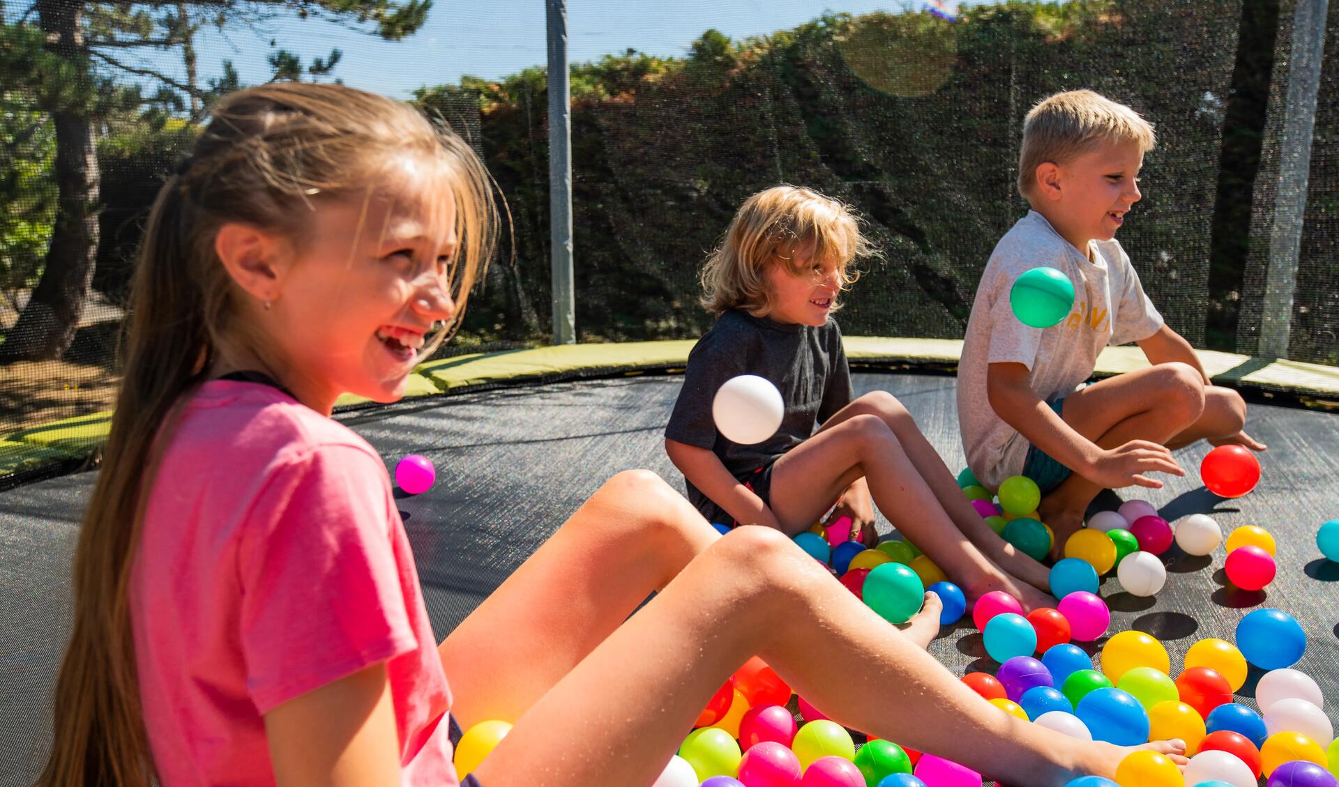 dzieci siedzące na trampolinie z rozsypanymi plastikowymi  kulkami