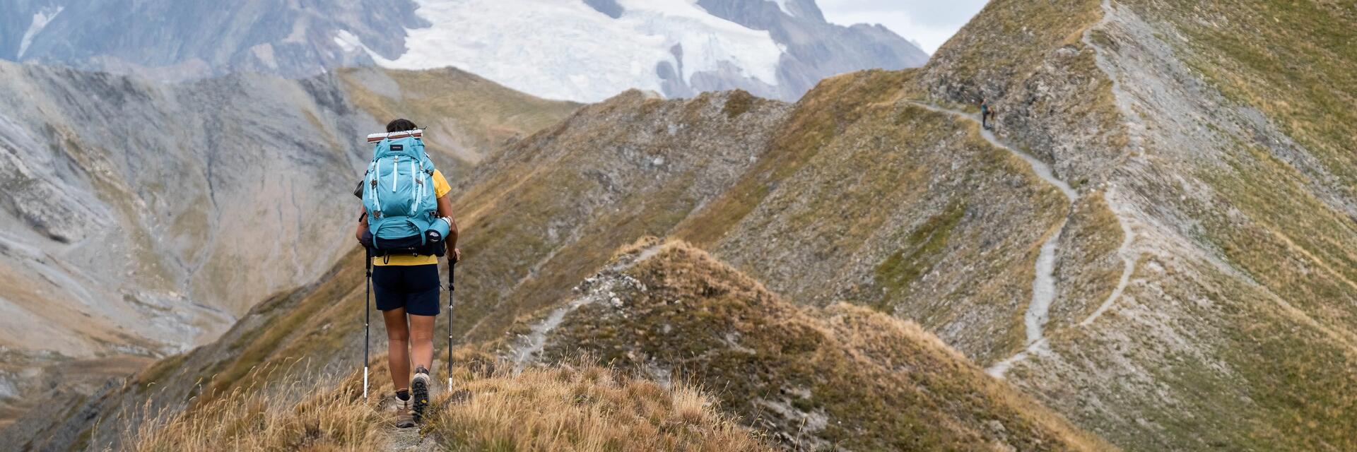 Kobieta idąca z ekwipunkiem górskim zapakowanym w niosący na plecach plecak turystyczny