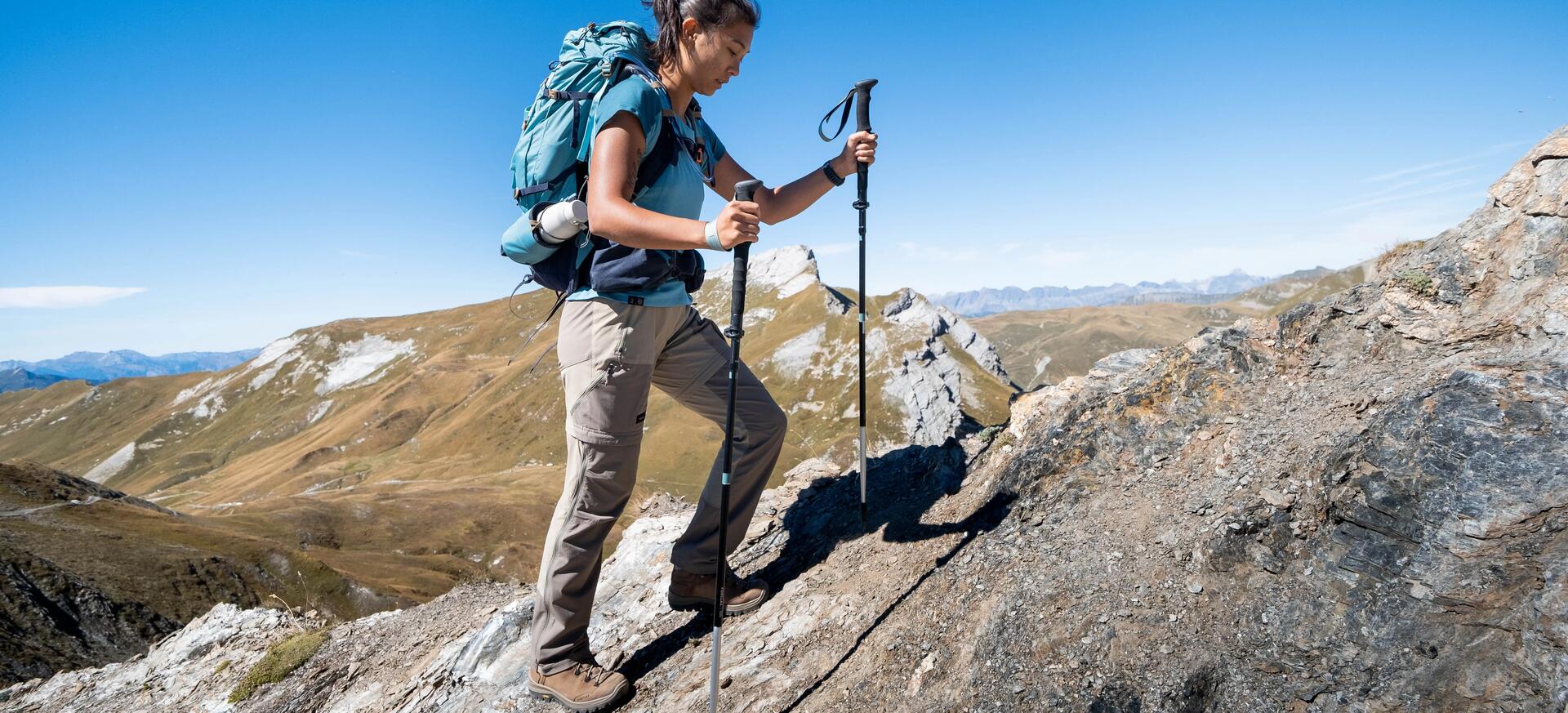 kobieta idąca po skale w butach trekkingowych z kijami trekkingowymi w rękach