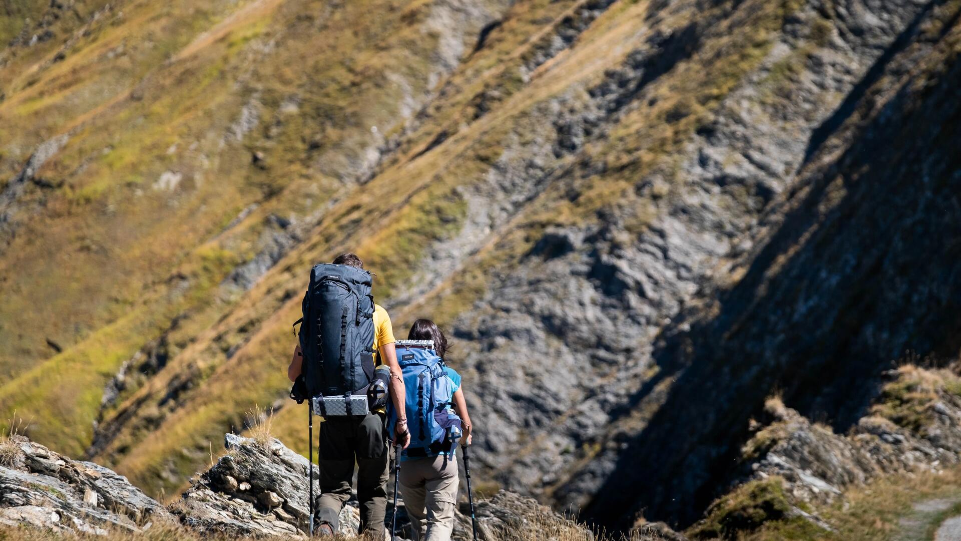 kobieta i mężczyzna wędrujący po górach z plecakami turystycznymi i kijami trekkingowymi