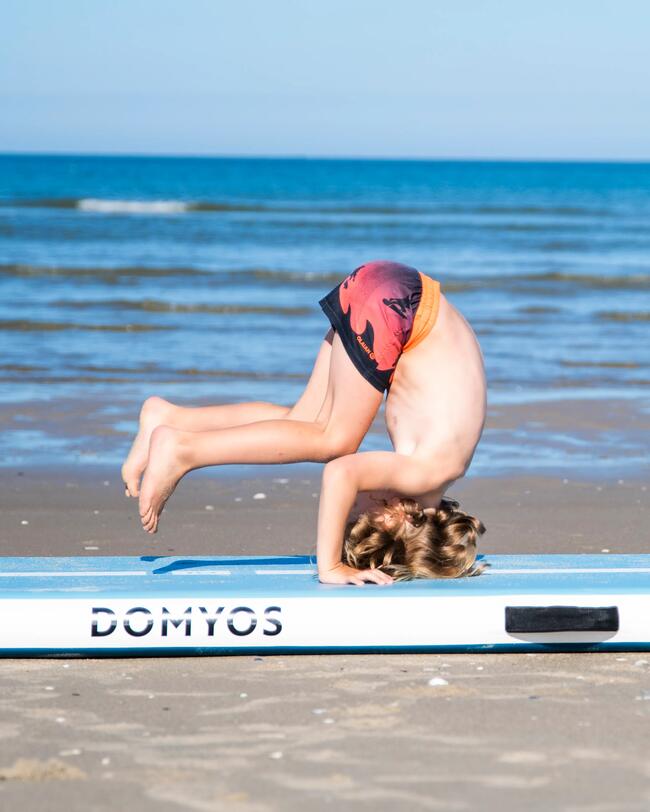 Ein Junge macht eine Rolle auf einer Turnmatte am Strand.