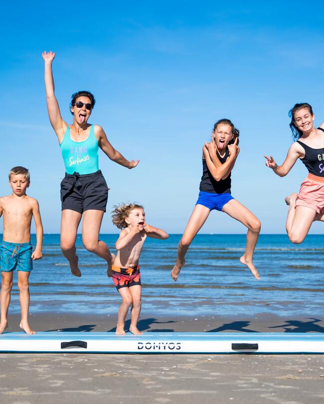 Eine Familie springt auf einer Turnmatte am Strand.