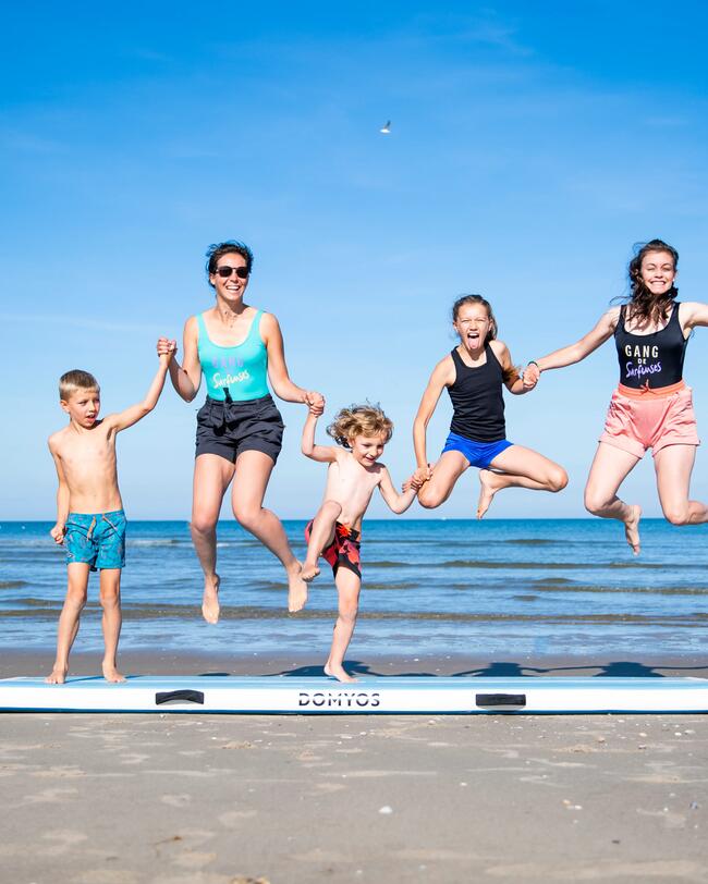 Eine Familie springt auf einer Turnmatte am Strand.