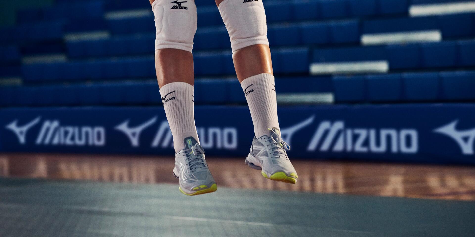 Wyskok kobiety grającej w siatkówkę w butach sportowych i nakolanikach