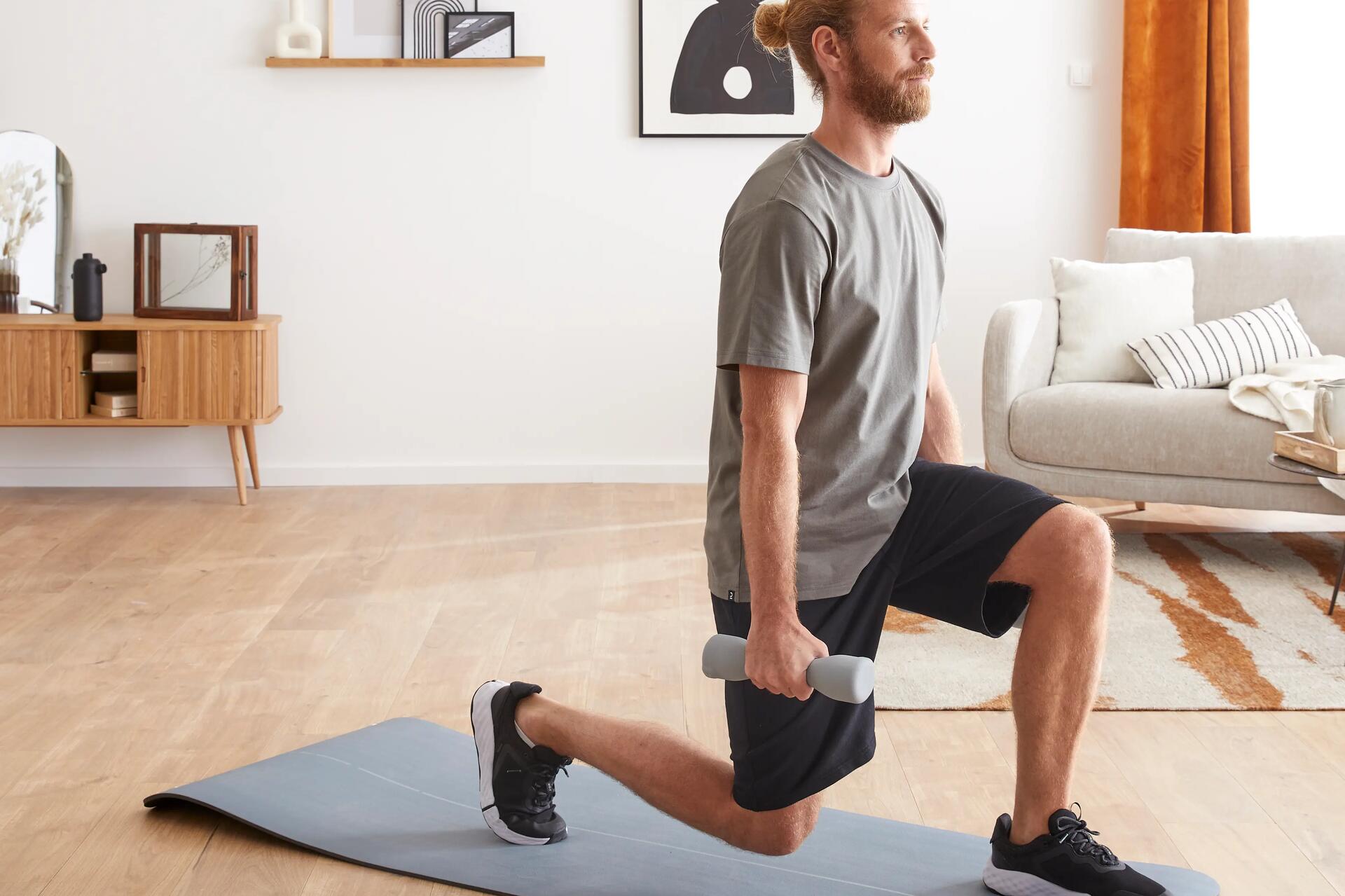 Mężczyzna w odzieży fitness wykonujący zakroki z hantlami na macie