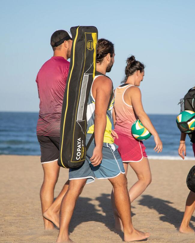 Personen am Strand trägt Beachvolleyballnetz-Set, blauem Himmel, brauner Sand, bunte Kleidung, ruhiges Meer im Hintergrund.