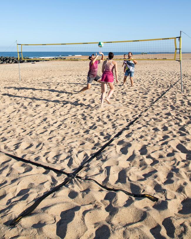Sandstrand mit gelbem Beachvolleyballnetz und schwarzen Spielfeldlinien, blauer Himmel im Hintergrund.