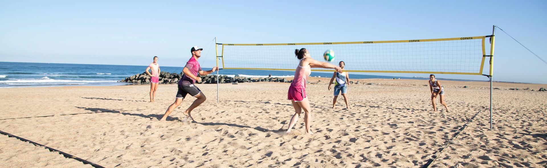 Grupa znajomych w strojach sportowych gra w siatkówkę plażową