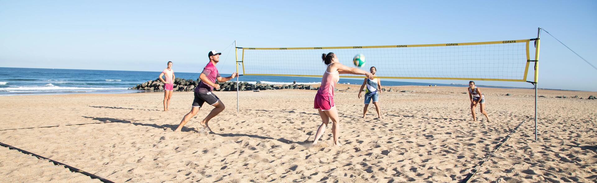 Grupa znajomych w strojach sportowych gra w siatkówkę plażową 