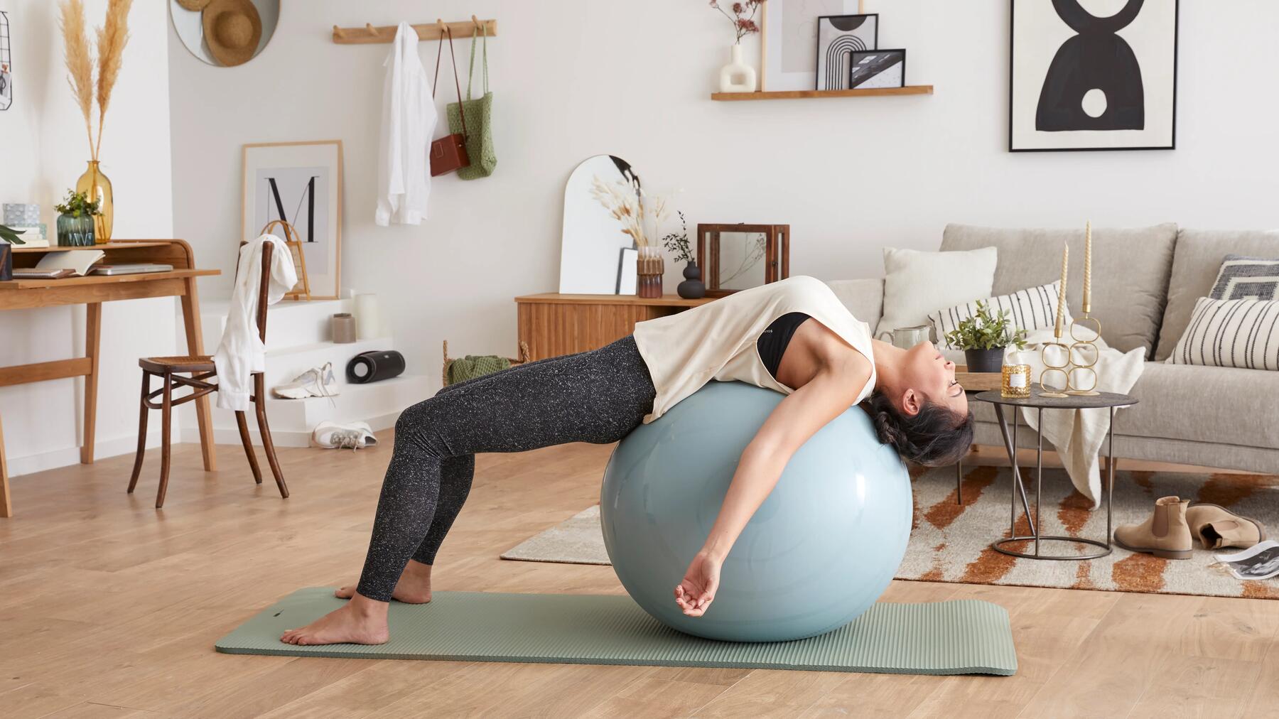 Kobieta w odzieży sportowej wykonująca stretching w domu z użyciem piłki 