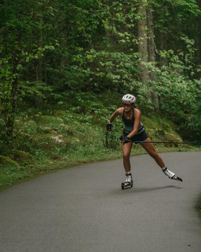 Frau fährt auf den Rollerski XC S SR Skate 500 durch Waldlandschaft auf Asphalt.