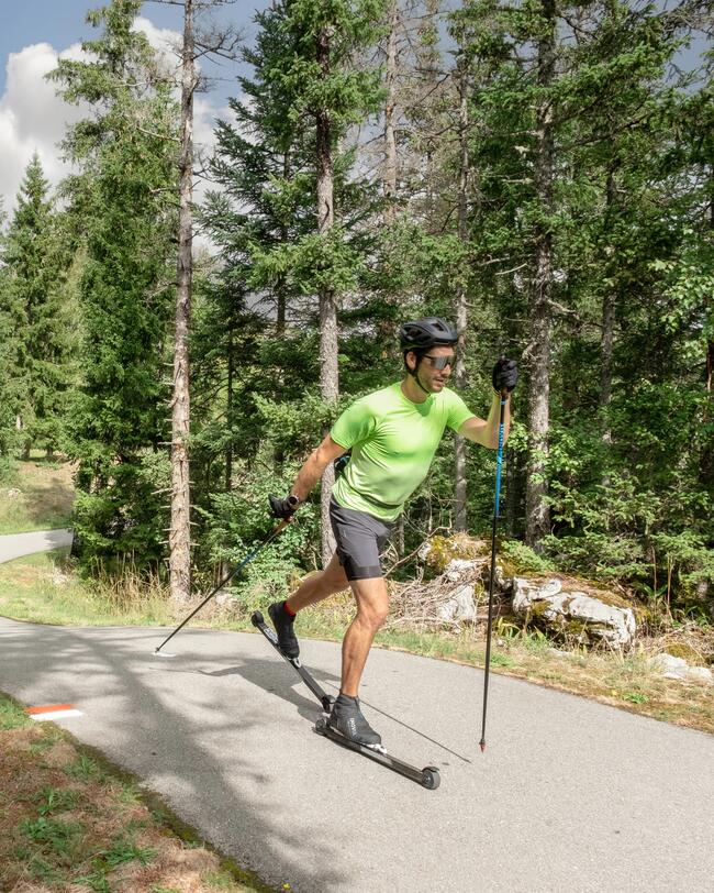 Ein Mann in sommerlicher Bekleidung fährt in Waldumgebung auf Asphalt mit seinen Rollerski.