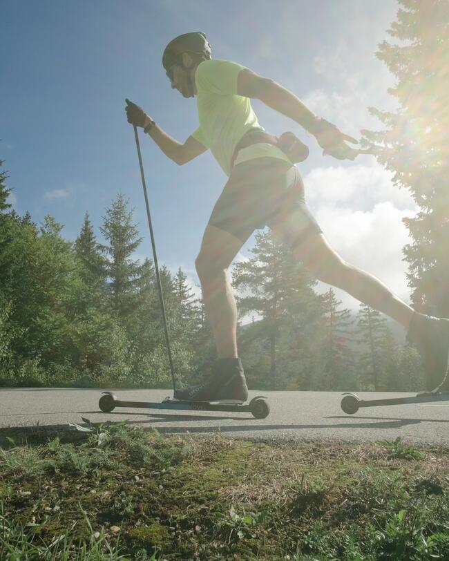 Mann in sommerlicher Kleidung fährt auf Asphalt Rollerski.