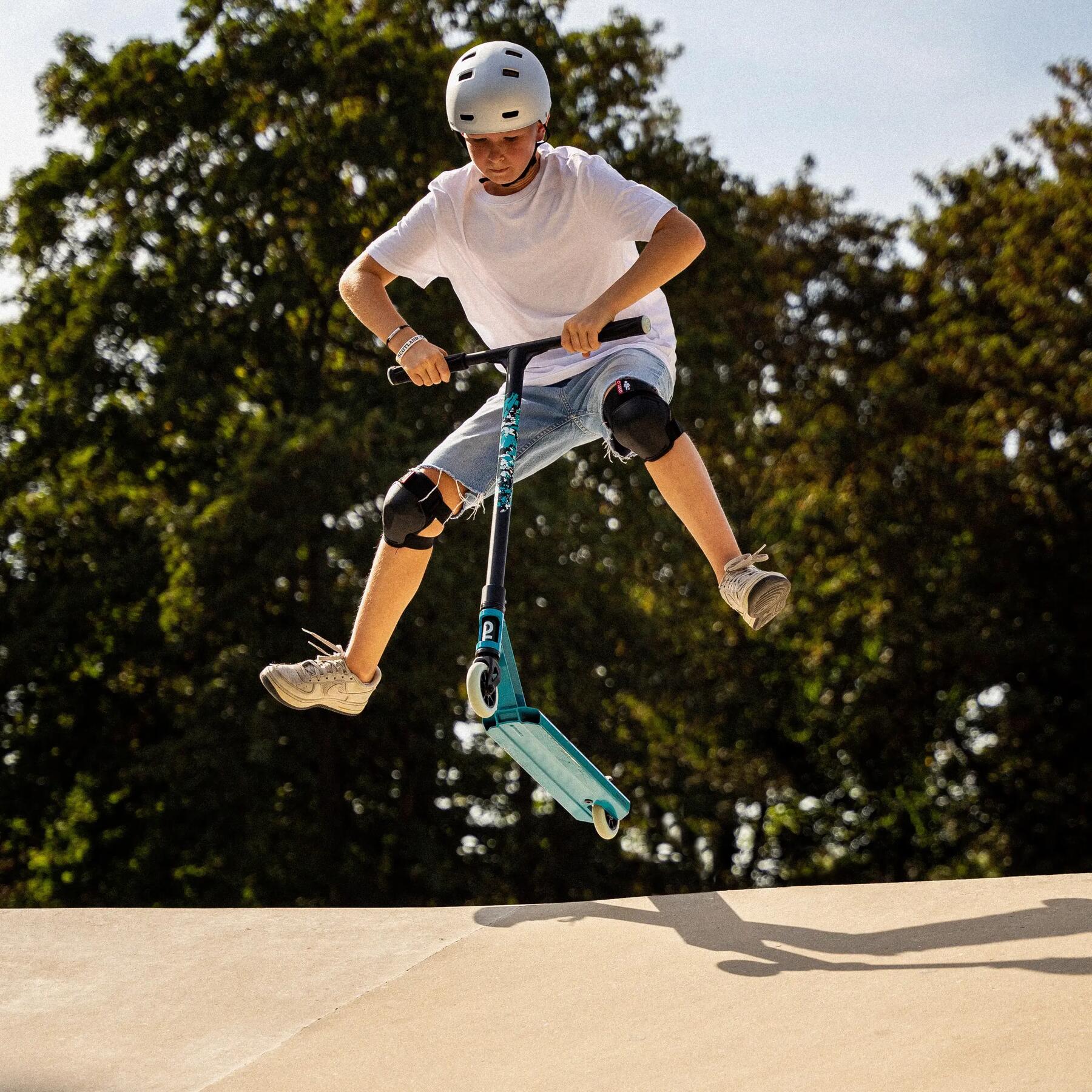 Chłopiec skaczący na hulajnodze wyczynowej z białymi kołami na skateparku