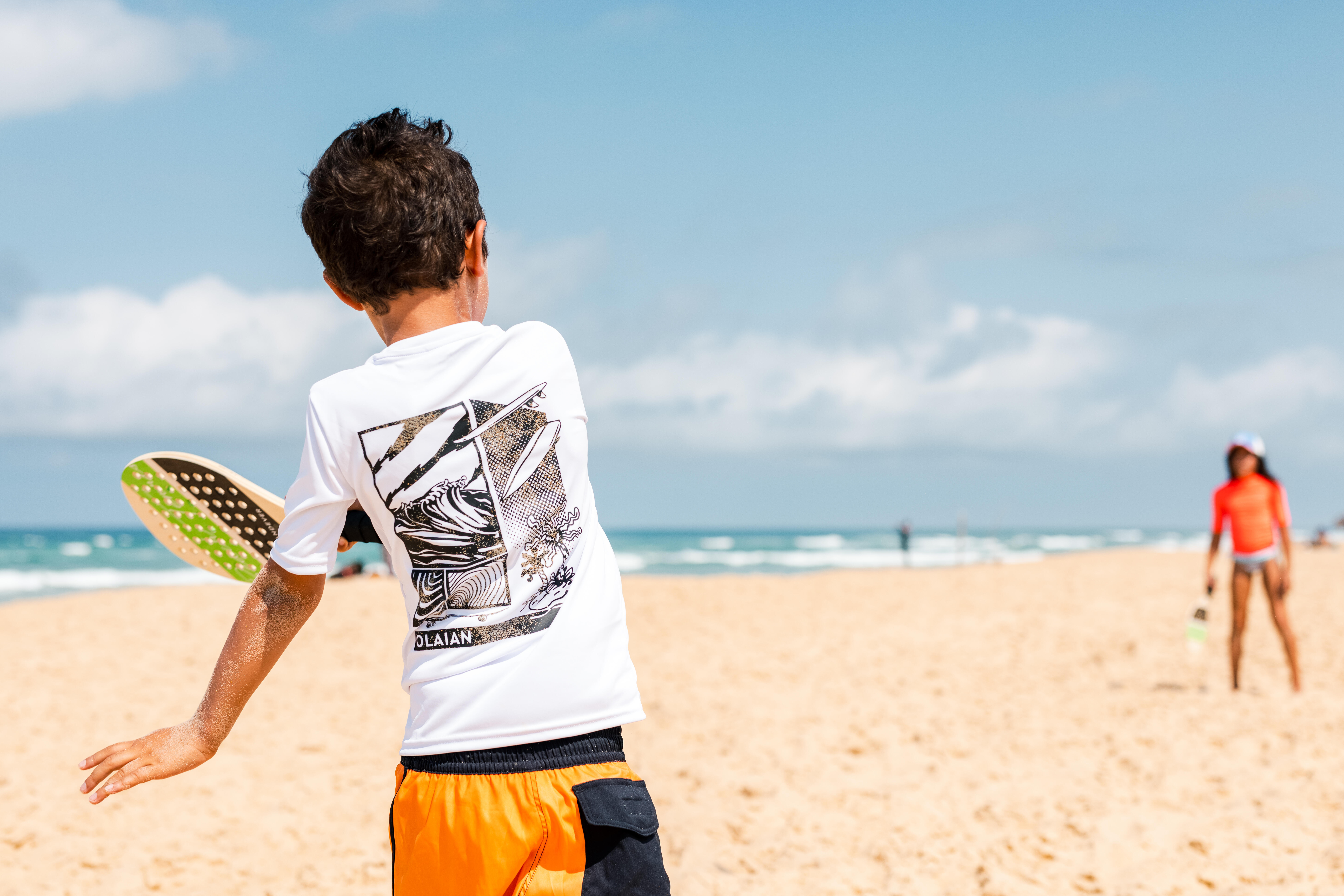 Child playing beach paddle ball on the sand.