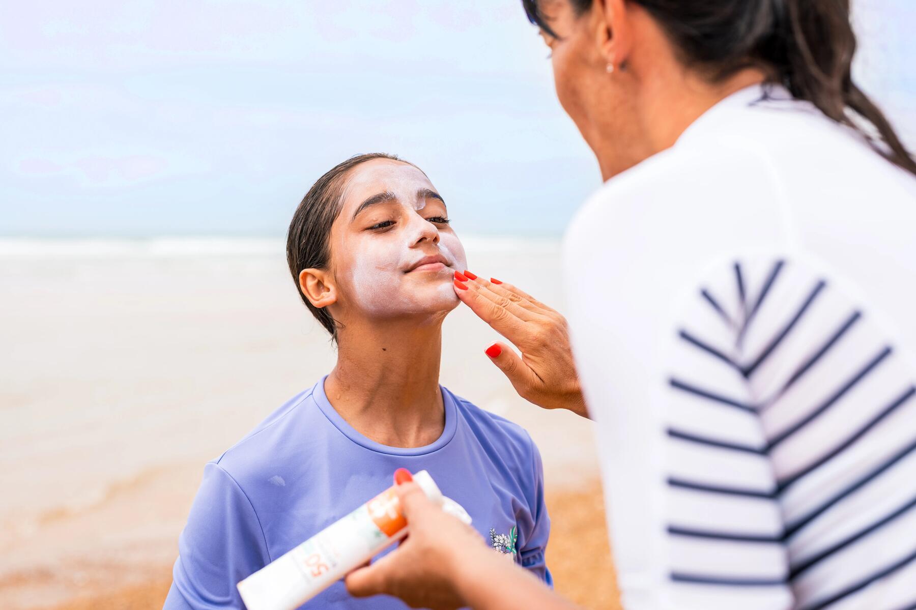 mujer echando crema solar a niña