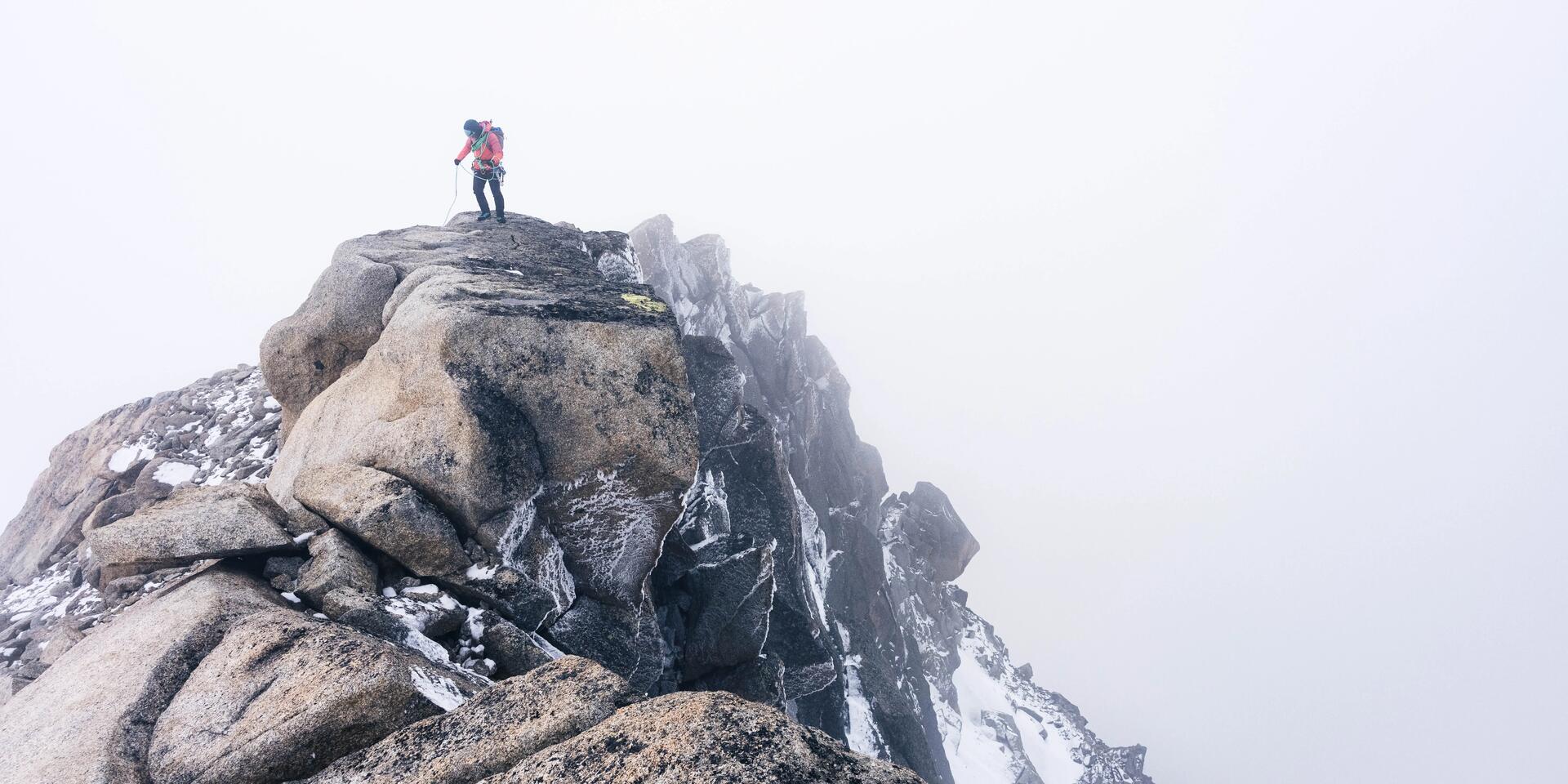 osoba stojąca na szczycie góry w odzieży alpinistycznej 