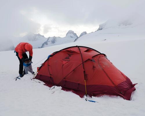 mężczyzna pakujący plecak przed namiotem w górach zimą