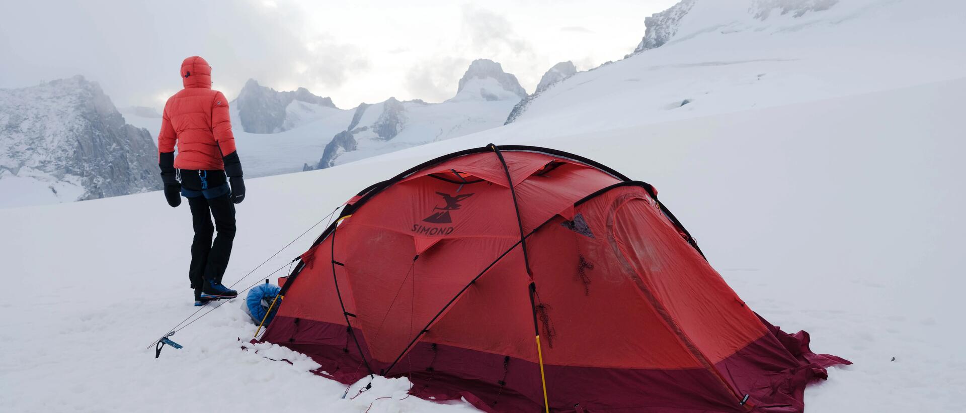 mężczyzna stojący zimą w górach przed namiotem