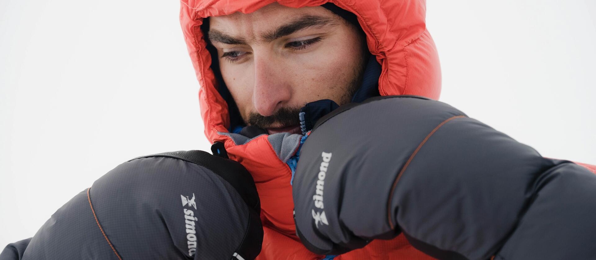 mężczyzna w kurtce alpinistycznej z łapawicami na dłoniach