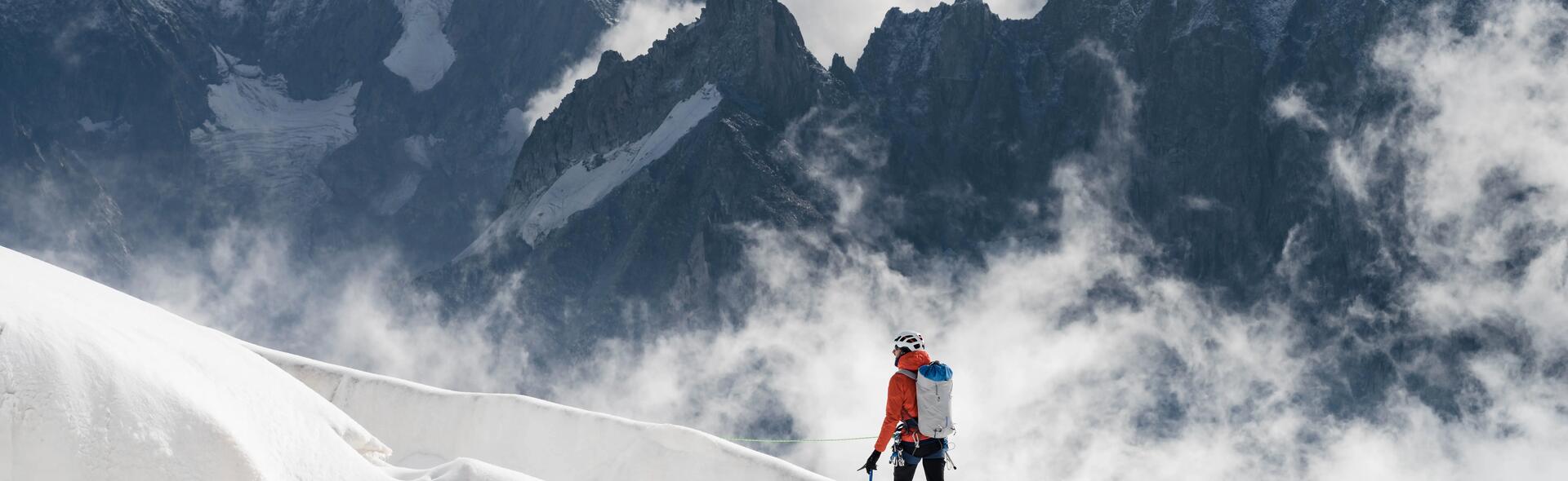 osoba wędrująca po wysokich górach w kasku i odzieży alpinistycznej