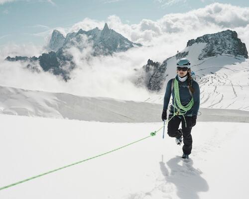 Kobieta w kasku z założoną uprzężą uprawiająca trekking pod lodowiec
