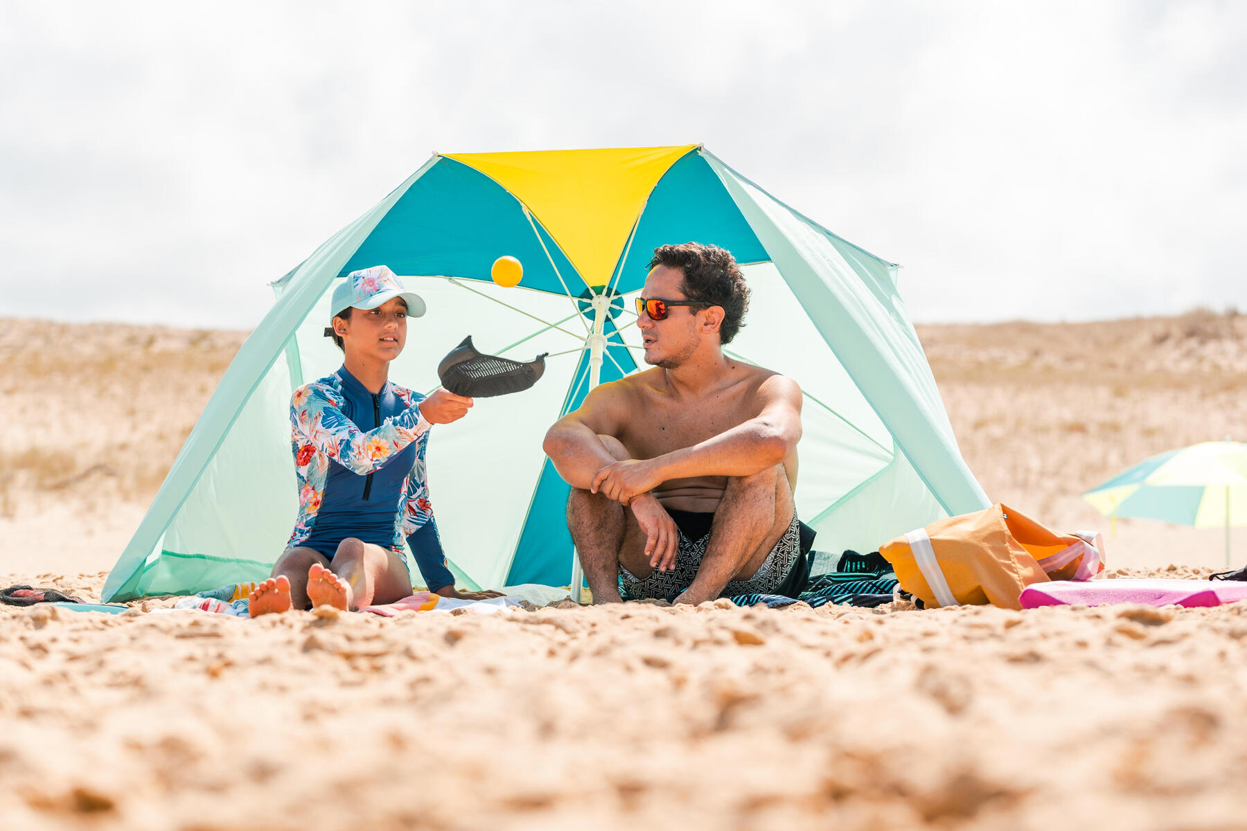Mężczyzna z dziewczynką siedzący pod parasolem na plaży