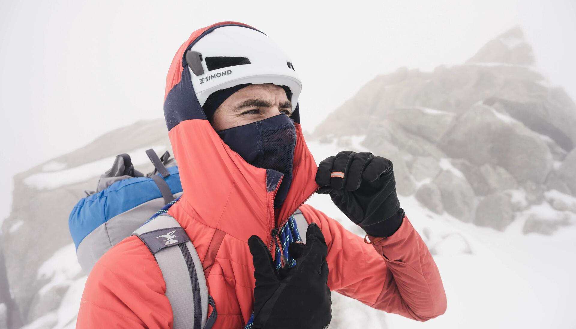 mężczyzna w kasku i odzieży alpinistycznej stojący w górach