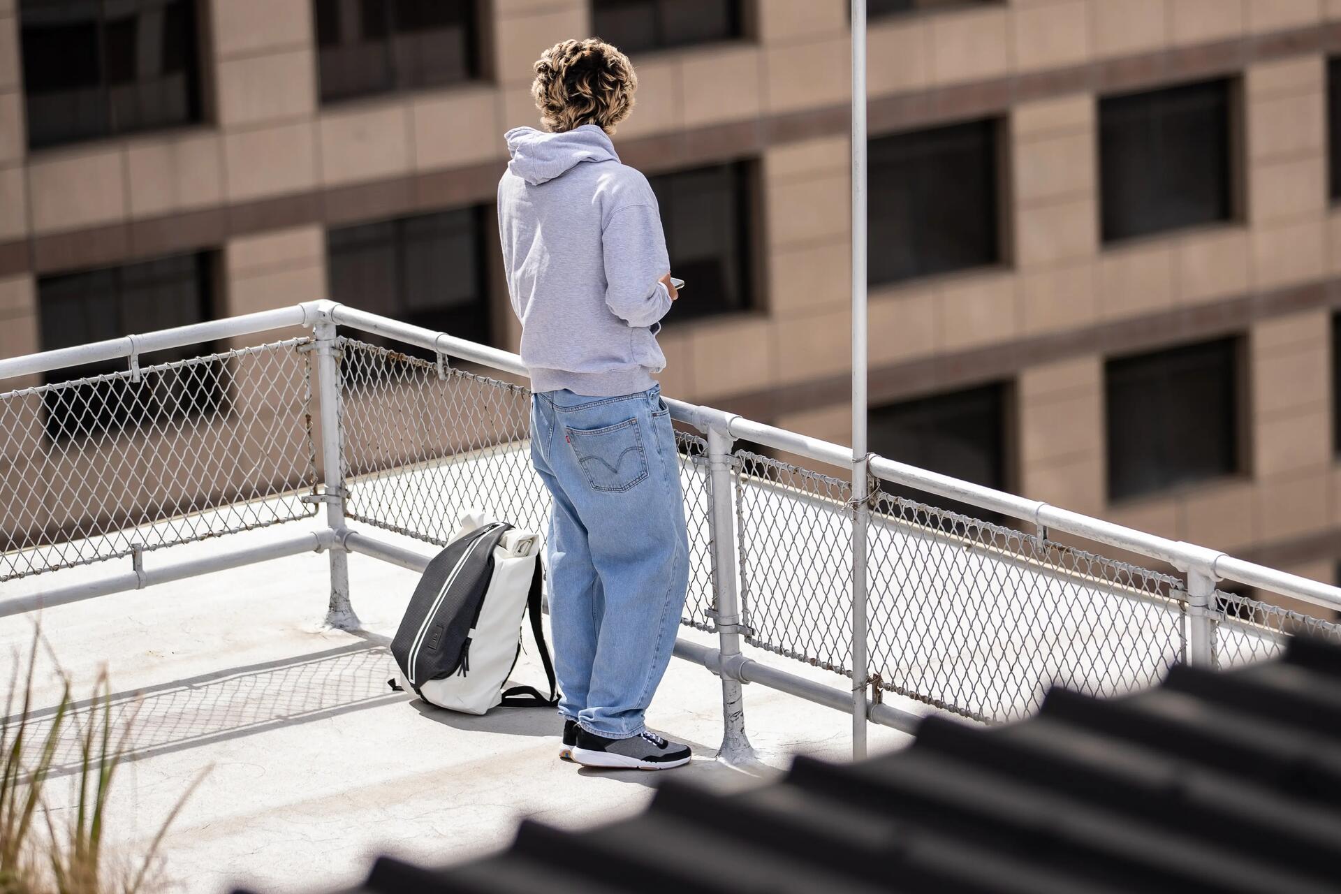 Chłopak w bluzie sportowej stojący obok leżącego na ziemi plecaka do szkoły średniej