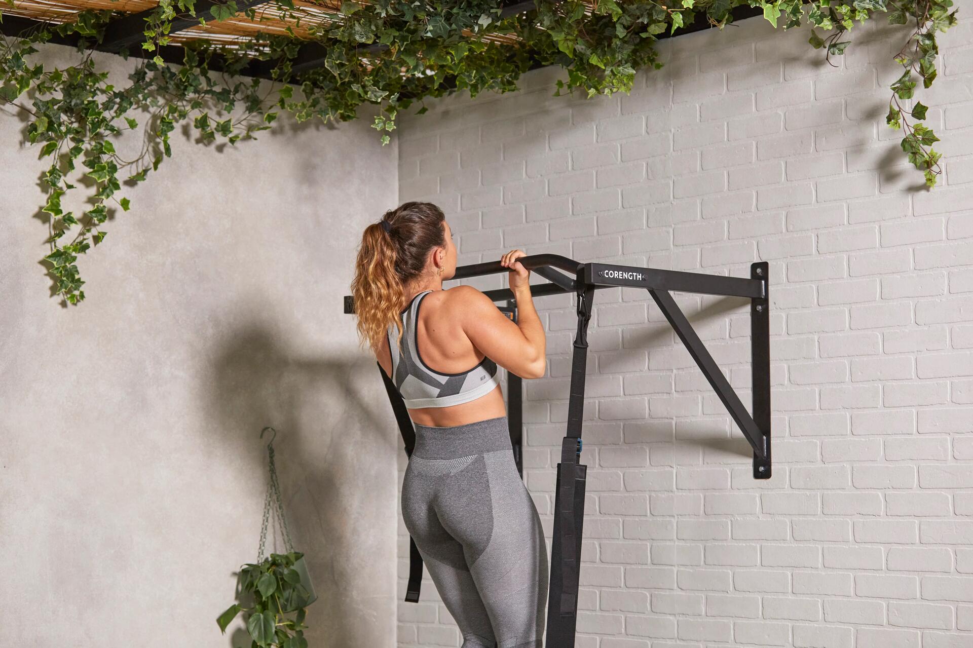 Kobieta w legginsach i staniku sportowym podciągająca się na drążku podczas treningu przed wspinaczką