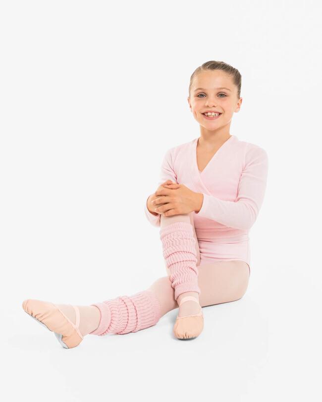 Ein Mädchen trägt ein rosa Ballettoutfit und sitzt auf dem Boden.