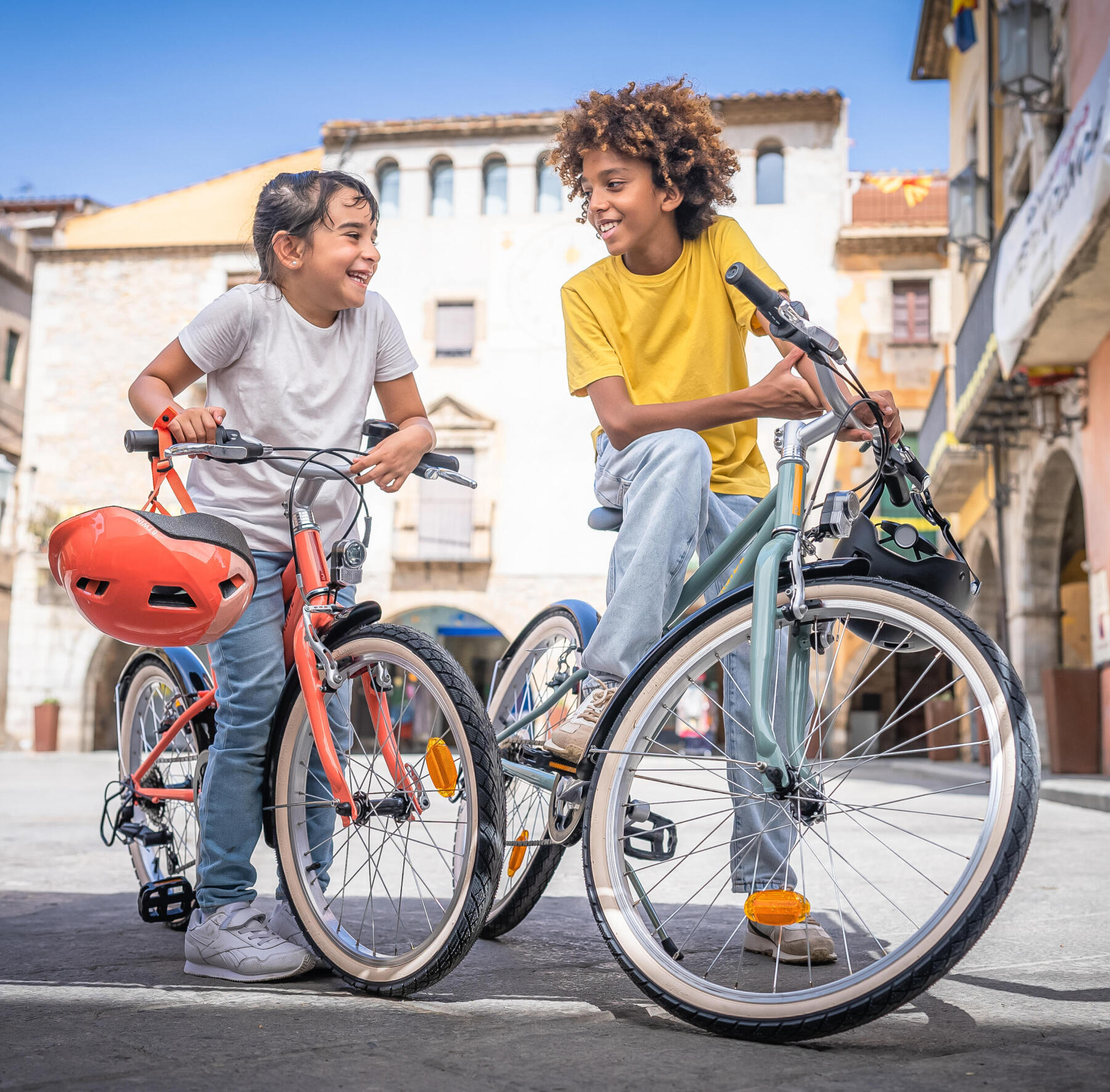 En pojke och en flicka står över sina cyklar och skrattar på ett torg.