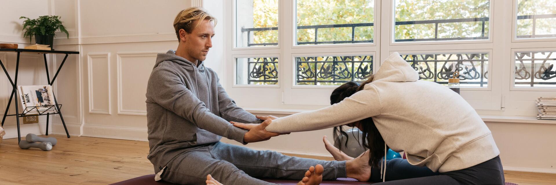 Ein Mann und eine Frau sitzen auf einer Yogamatte und dehnen ihren oberen Rücken