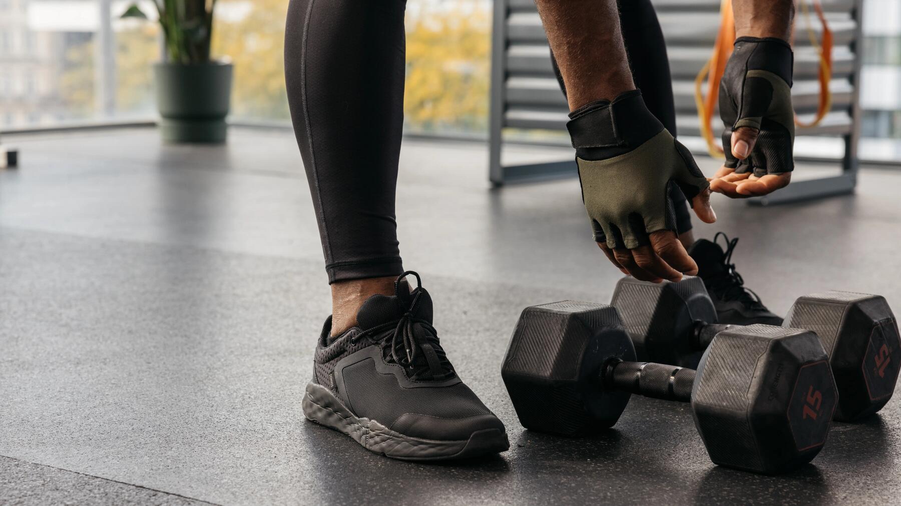 Osoba w butach sportowych i rękawiczkach fitness schylająca się po hantle