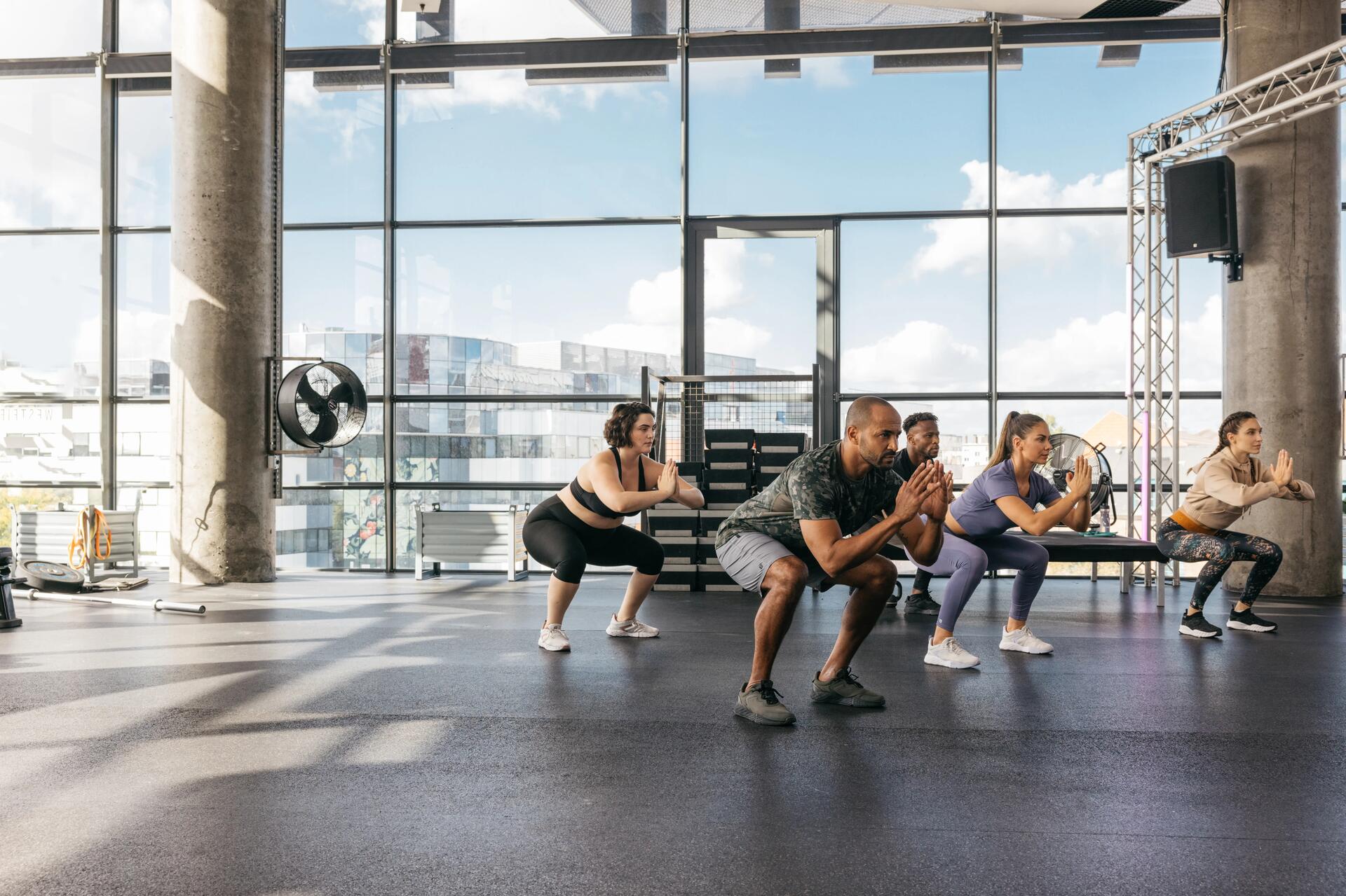 Kobiety i mężczyźni w odzieży fitness trenujący tabatę wykonujac przysiady na sali treningowej