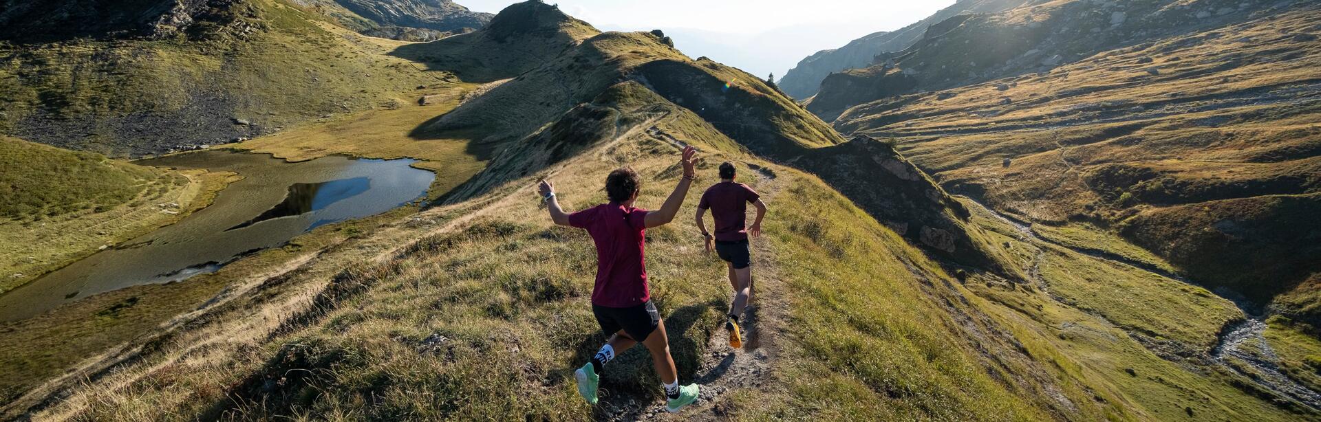 man and woman running on a scenic green mountain trail