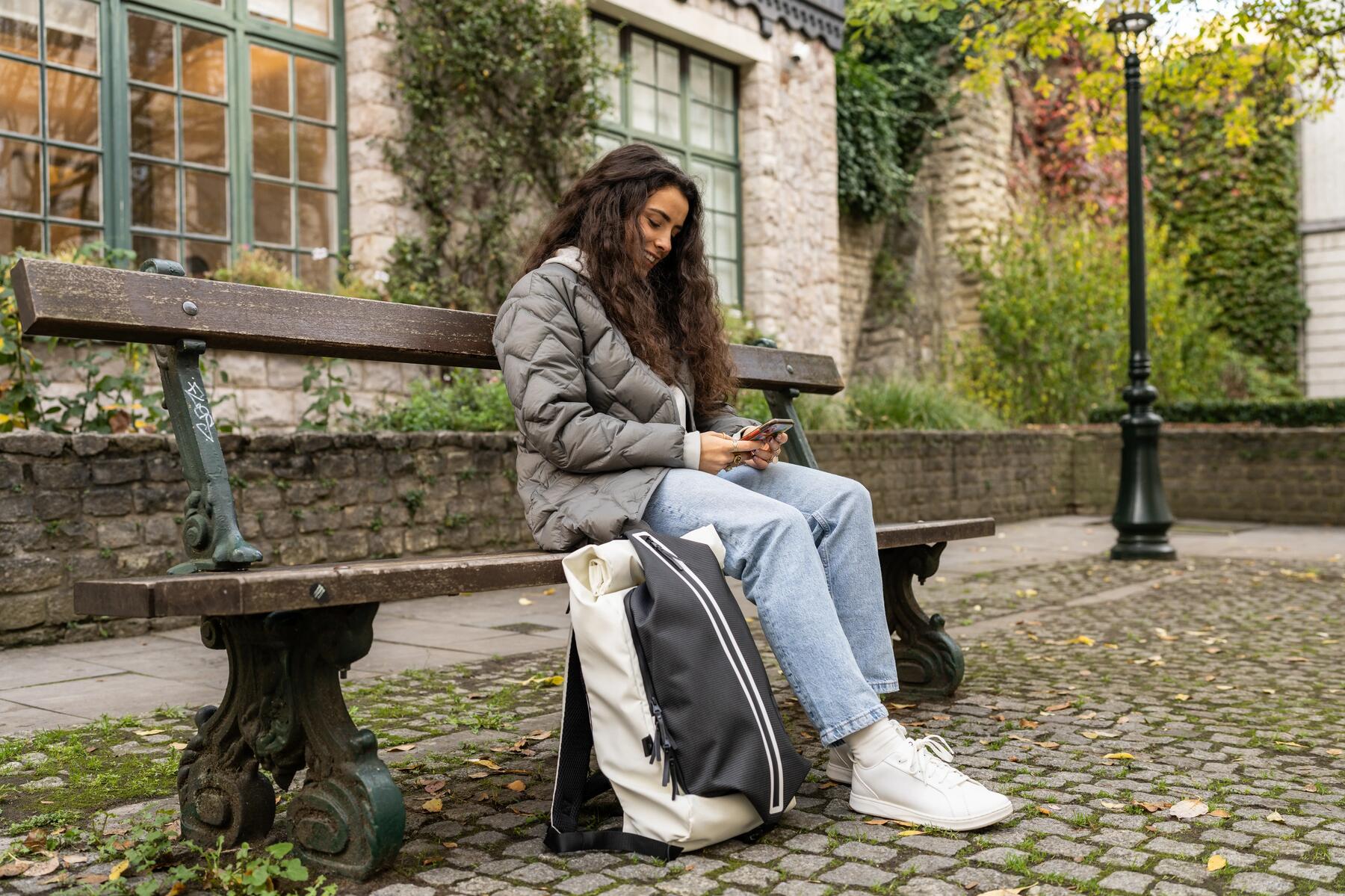 Dziewczyna siedząca na ławce obok leżącego na ziemi plecaka do liceum