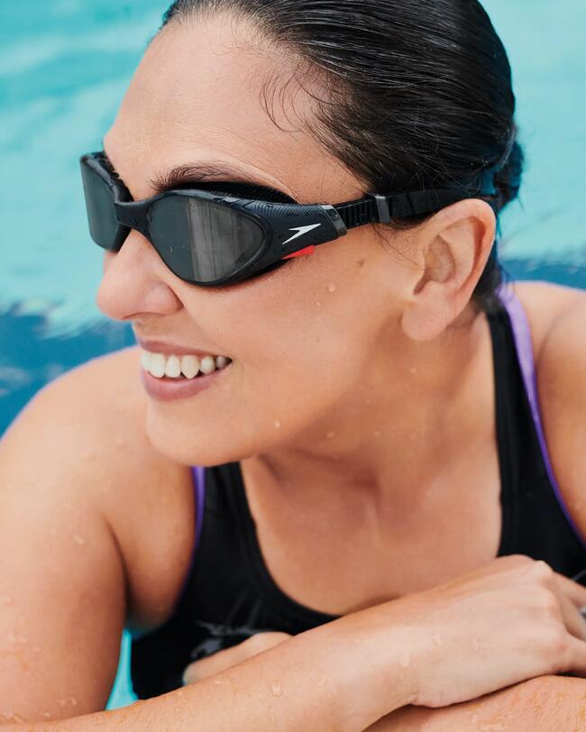 Vrouw leunt lachend aan de rand van het zwembad met een Speedo biofuse zwembril op