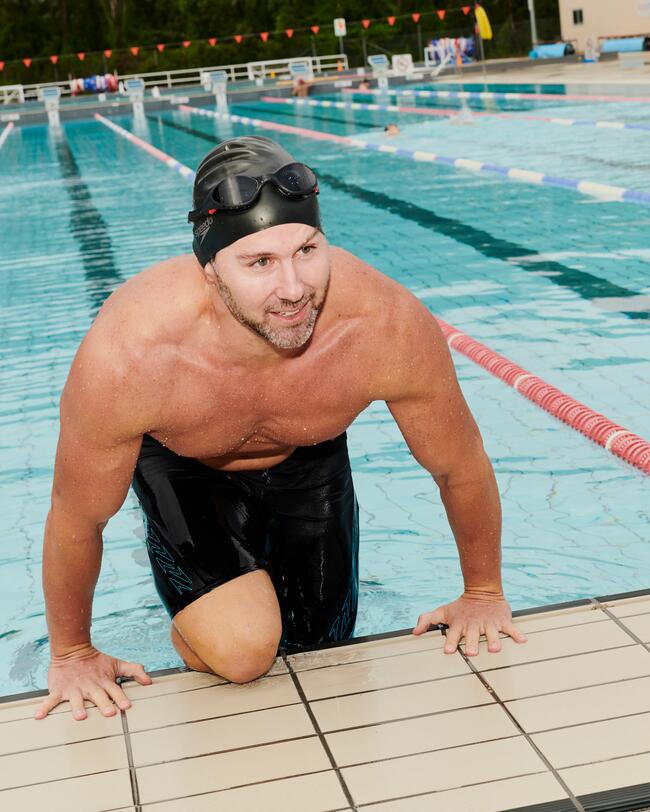 Man met een Speedo biofuse zwembril op klimt lachend op de rand van het zwembad