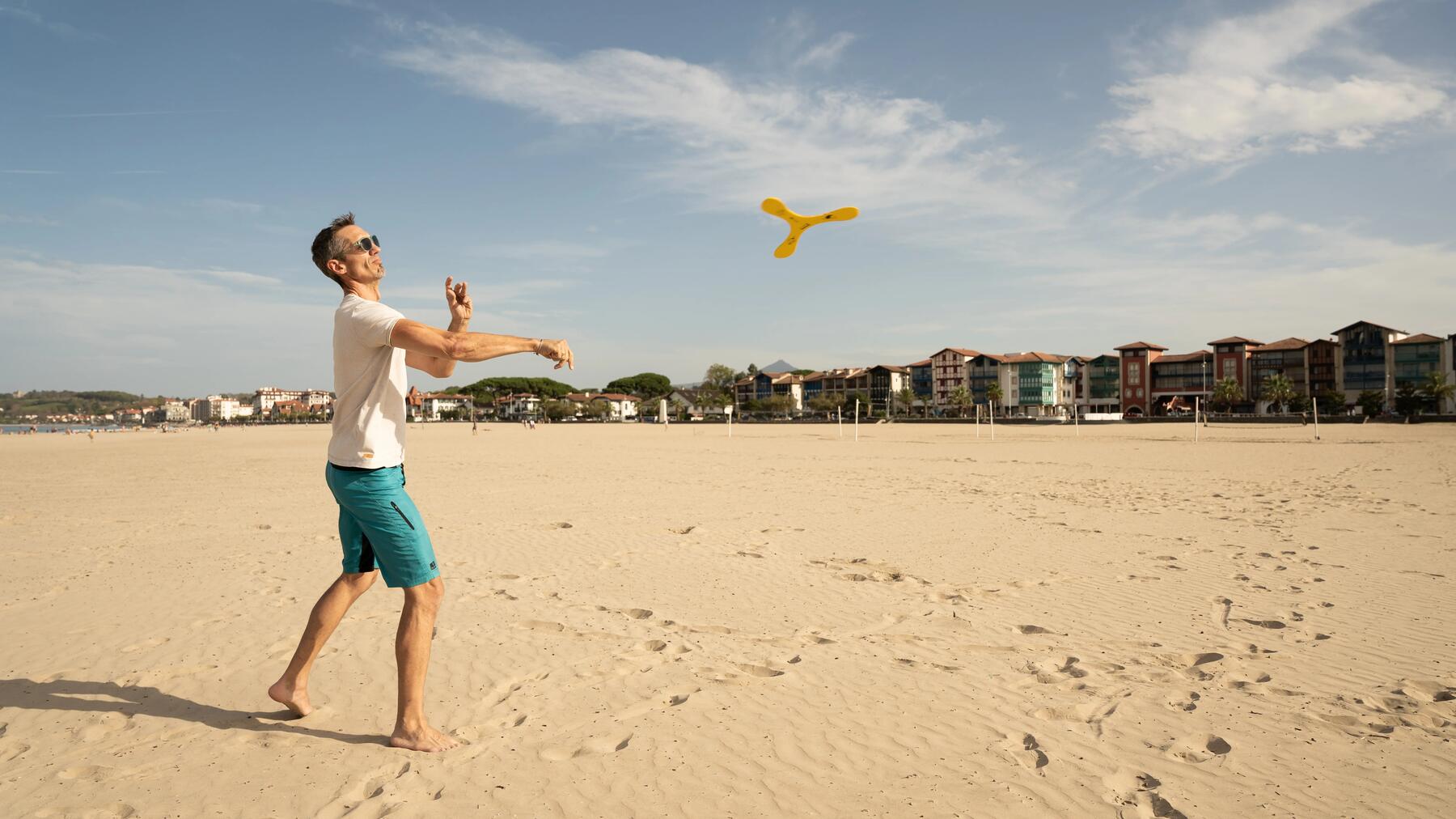 Ein Mann in sportlicher Pose wirft am Sandstrand kraftvoll einen Bumerang