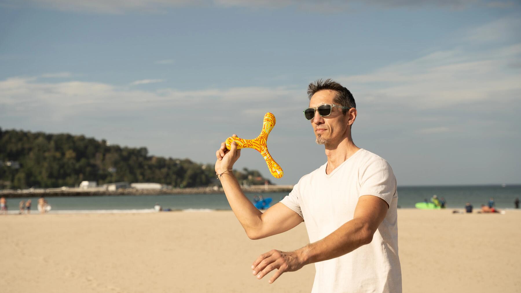 Ein Mann am Strand wirft konzentriert einen Bumerang