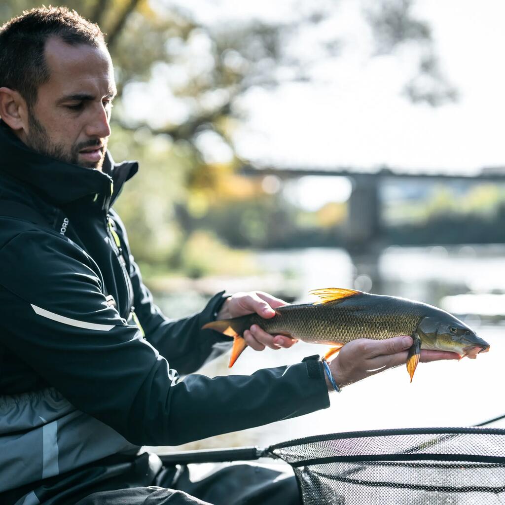 EIn Angler sitzt mit seiner angel am wasser und präsentiert eine gefangene Barbe