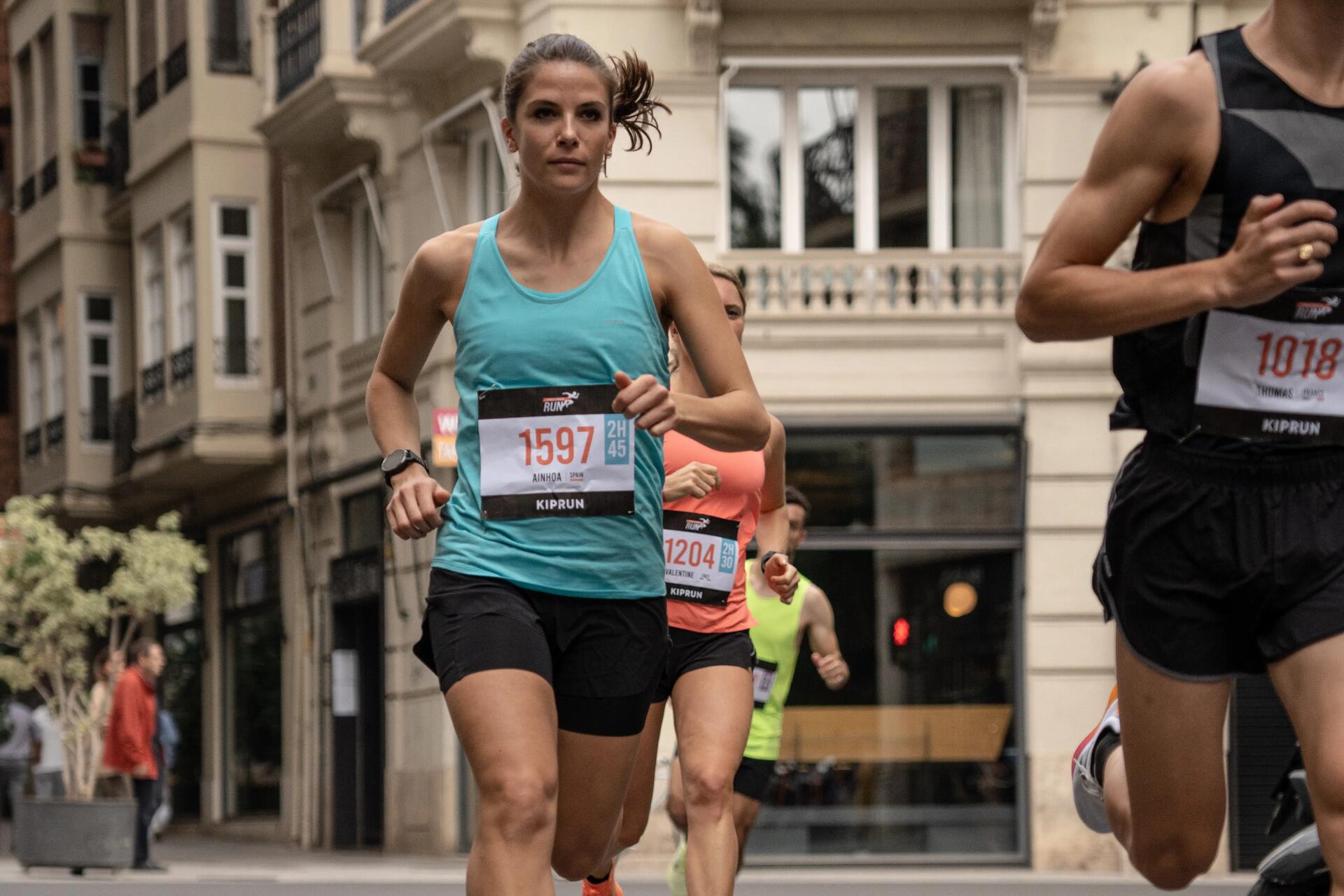 Kobieta w odzieży do biegania biorąca udział w maratonie biegnąc z innymi zawodnikami ulicą